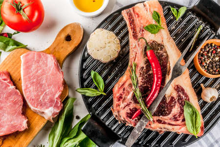 Raw beef marbled meat striplon rib eye steak with pork steaks spices, grill pan, and herbs, white marble background top view, copy spaceの写真素材