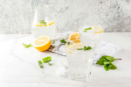 Summer refreshing drinks, mojito or lemonade with fresh mint, slices of lemon, ice, on a light...