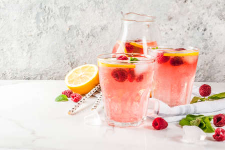 Summer refreshing drinks, fruit and berry raspberry mojito or lemonade with fresh mint, frozen raspberries, slices of lemon, ice, on a light background. copy spaceの写真素材