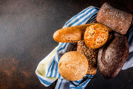 Variety of fresh homemade grain bread, in a metal basket, dark rusty background copy space top view