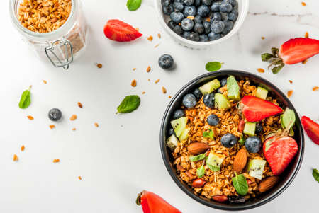Healthy breakfast with muesli or granola with nuts and fresh berries and fruits - strawberry, blueberry, kiwi, on white table, copy space top viewの写真素材