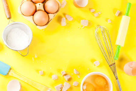 Ingredients and utensils for cooking baking egg, flour, sugar, whisk, rolling pin, on bright yellow background, copy space top view frameの写真素材