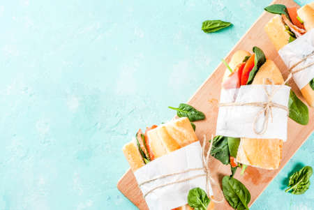 Fresh baguette sandwich with bacon, cheese, tomatoes and spinach, light blue background copy space...