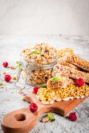 Healthy breakfast and snack concept, homemade granola with fresh raspberries in jar and nuts and granola bars, on grey stone stone background copy spaceの写真素材