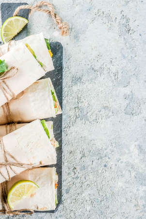 Healthy lunch snack. Stack of mexican street food fajita tortilla wraps with grilled buffalo chicken fillet and fresh vegetables, light grey background copy spaceの写真素材