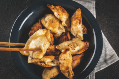 Fried asian dumplings Gyoza  on dark plate, served with chopsticks and soy sauce, dark background,...