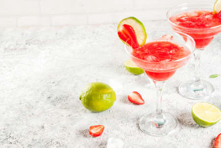 Cold strawberry margarita cocktail with ice, lime and fresh berries in margarita glass, light grey...