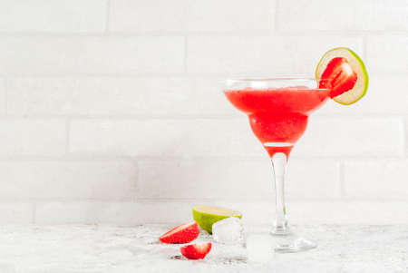 Cold strawberry margarita cocktail with ice, lime and fresh berries in margarita glass, light grey background copy spaceの写真素材