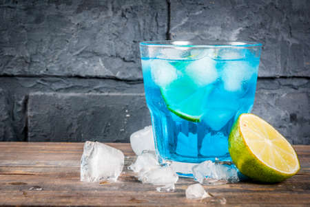 Colorful summer beverage, iced blue  alcohol cocktail drink with lime and mint, bark background copy spaceの写真素材
