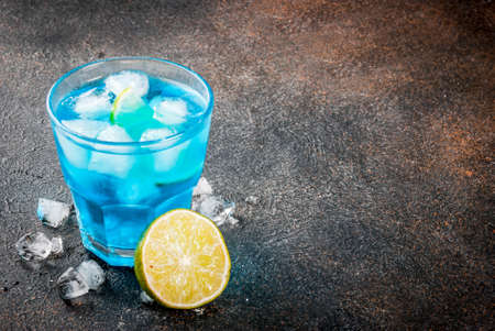 Colorful summer beverage, iced blue alcohol cocktail drink with lime and mint, bark background copy spaceの写真素材