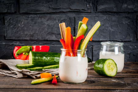 Summer healthy snack appetizer, assorted colorful fresh vegetable sticks (celery, rhubarb, pepper, cucumber and carrot) with yoghurt sauce dip, wood and dark concrete background copy spaceの写真素材