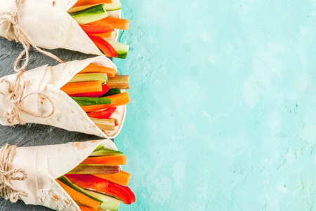 Summer healthy snack, Mexican style tortilla sandwich wraps assorted colorful fresh vegetable sticks (celery, rhubarb, pepper, cucumber and carrot) with yoghurt sauce dip light blue backgroundの写真素材