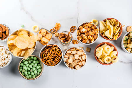 Variation different unhealthy snacks crackers, sweet salted popcorn, tortillas, nuts, straws,...