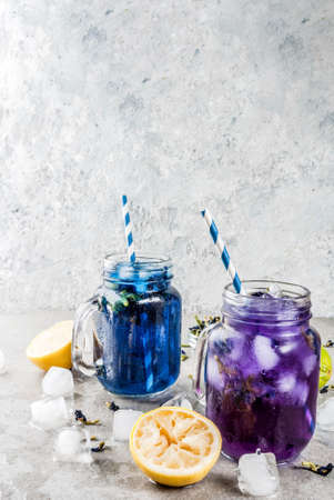 Healthy summer cold beverage, iced organic blue and violet butterfly pea flower tea with limes and lemons, grey concrete background copy space top viewの写真素材