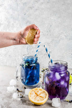 Healthy summer cold beverage, iced organic blue and violet butterfly pea flower tea with limes and lemons, grey concrete background copy space top viewの写真素材
