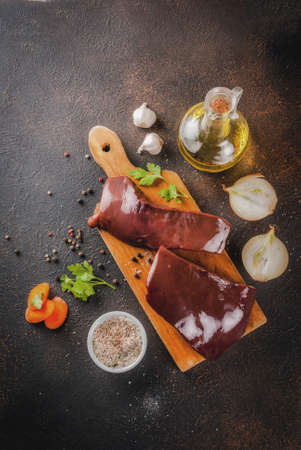 Raw beef liver with spices, herbs and vegetables, dark rusty table copy space top viewの写真素材