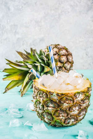 Summer refreshment drink concept, tropical pineapple cocktail or juice in pineapple with ice, light blue concrete background copy spaceの写真素材