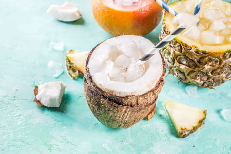 Summer holiday drink concept, set various tropical cocktails or juices in pineapple, grapefruit and coconut with ice, light blue concrete background copy spaceの写真素材