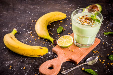 Healthy summer drink, avocado and banana smoothie with lime, granola and coconut milk, dark rusty background copy spaceの写真素材