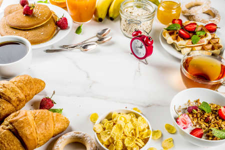 Healthy breakfast eating concept, various morning food - pancakes, waffles, croissant oatmeal sandwich and granola with yogurt, fruit, berries, coffee, tea, orange juice, white backgroundの写真素材