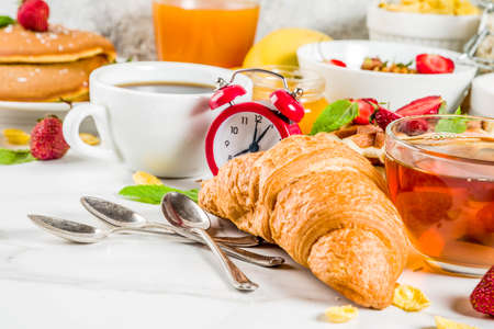 Healthy breakfast eating concept, various morning food - pancakes, waffles, croissant oatmeal sandwich and granola with yogurt, fruit, berries, coffee, tea, orange juice, white backgroundの写真素材