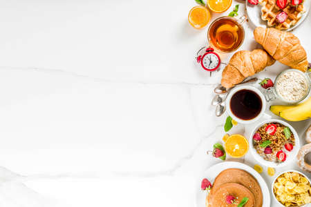 Healthy breakfast eating concept, various morning food - pancakes, waffles, croissant oatmeal sandwich and granola with yogurt, fruit, berries, coffee, tea, orange juice, white backgroundの写真素材