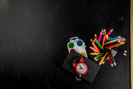 Back to school concept with books, alarm clock, color pencils, chalkboard backgroundの写真素材