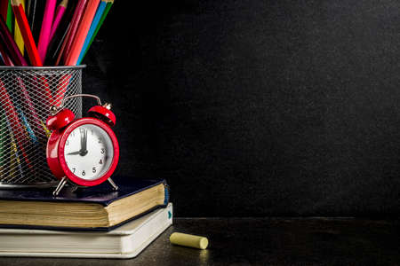 Back to school concept with books, alarm clock, color pencils, chalkboard background