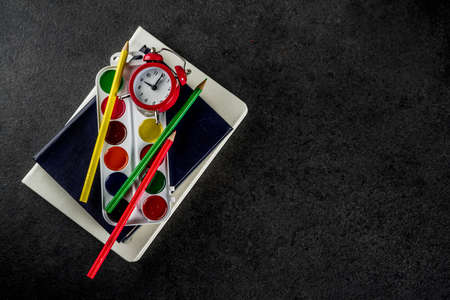 Back to school concept with books, alarm clock, color pencils, chalkboard backgroundの写真素材