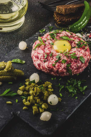 French cuisine, beef steak tartare with raw quail egg yolk, pickled cucumber and onions, fresh herbs, bread, dark rusty background copy spaceの写真素材