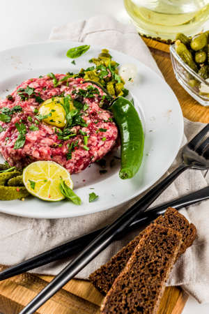 French cuisine, beef steak tartare with raw quail egg yolk, pickled cucumber and onions, fresh herbs, bread, white marble background copy spaceの写真素材