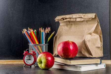 Healthy school food concept, paper bag with lunch, apple, sandwich, books and alarm clock on chalkboard background copy spaceの写真素材