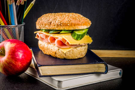 Healthy school food concept, lunch with apple, sandwich, books and alarm clock on chalkboard background copy spaceの写真素材