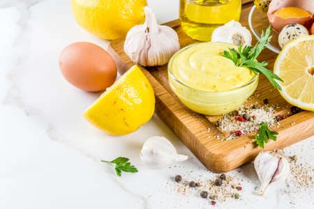 Homemade mayonnaise sauce with ingredients - lemon, eggs, olive oil, spices and herbs, white marble...