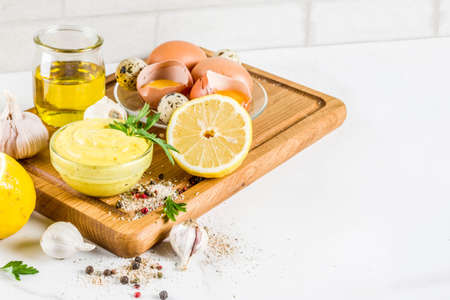 Homemade mayonnaise sauce with ingredients - lemon, eggs, olive oil, spices and herbs, white marble kitchen table copy spaceの写真素材