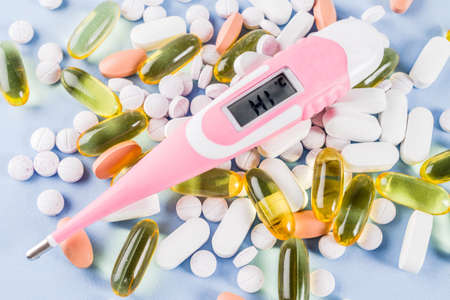 Medical and healthcare concept - different shape pills, thermometer on blue background, top viewの写真素材