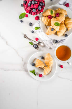 Sweet summer dessert, homemade baked mini croissants with berry jam, served with tea, fresh raspberries, blueberries and mint. On a white marble table, copy space top viewの写真素材