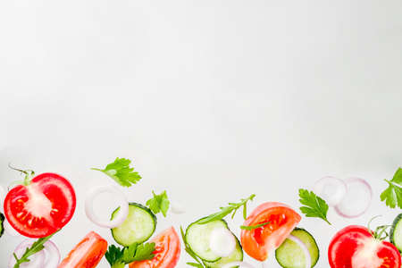 Creative background, layout, concept of fresh healthy diet of salad, fresh raw  vegetables tomatoes parsley onions cucumbers greens, simple pattern on white backgroundの写真素材