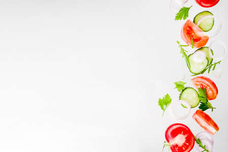 Creative background, layout, concept of fresh healthy diet of salad, fresh raw  vegetables tomatoes parsley onions cucumbers greens, simple pattern on white backgroundの写真素材