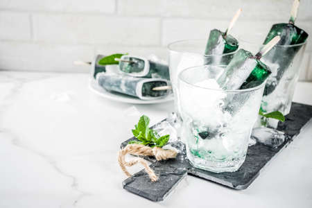 Trendy food, Asian vegan desserts, homemade ice cream popsicles with algae spirulina, served with mint in glasses with ice, white marble background copy spaceの写真素材