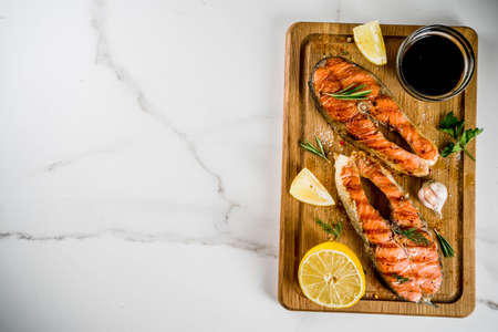 Grilled salmon fish steaks with ingredients lemon, herbs, olive oil, slate cutting board, dark rusty background copy spaceの写真素材