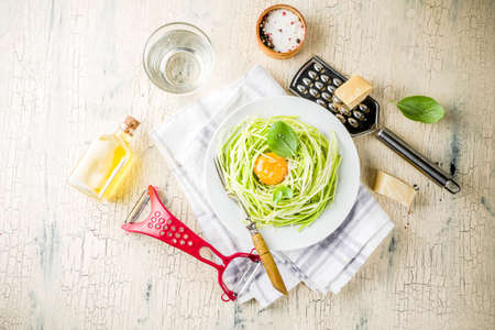 Trendy vegan food recipes, cheese zucchini spaghetti pasta with egg yolk with parmesan, olive oil and basil leaves, light concrete background copy spaceの写真素材