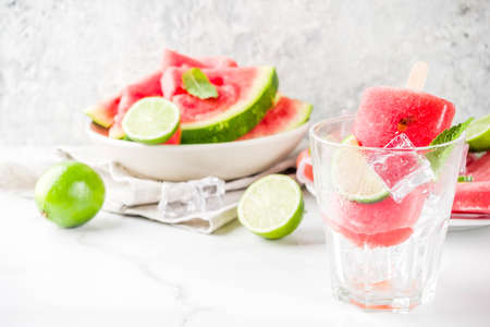 Sweet summer watermelon and lime popsicles with sliced watermelon and mint, on white marble background copy spaceの写真素材