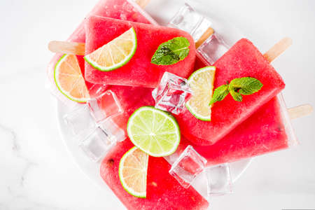 Sweet summer watermelon and lime popsicles with sliced watermelon and mint, on white marble...