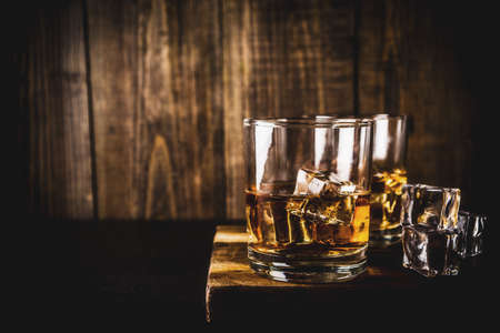 Two whiskey shot glasses on dark wooden background, with ice cubes, copy spaceの写真素材