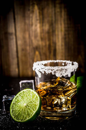 Two tequila shot glasses on dark background, with ice cubes, salt and limes copy spaceの写真素材