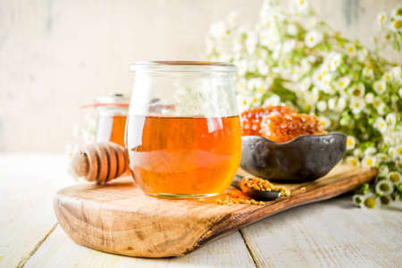 Organic floral honey, in jars, with pollen and honey combs, on a white wooden table, with...
