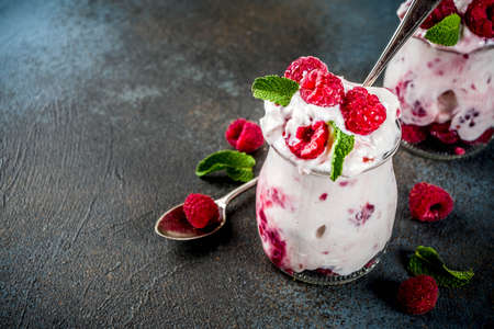 Healthy breakfast, cream dessert, frozen yogurt with fresh raspberries, raspberry jam, served with fresh mint leaves. On dark blue concrete background, copy spaceの写真素材