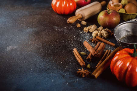 Sweet autumn baking cooking background with flour, rolling pin, decorative pumpkins, apples, cinnamon spices with anise cardamom sugar. Dark blue rusty background top view copy spaceの写真素材