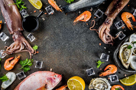 Fresh raw seafood squid shrimp oyster mussels fish with spices of herbs lemon on dark rusty background copy space top viewの写真素材